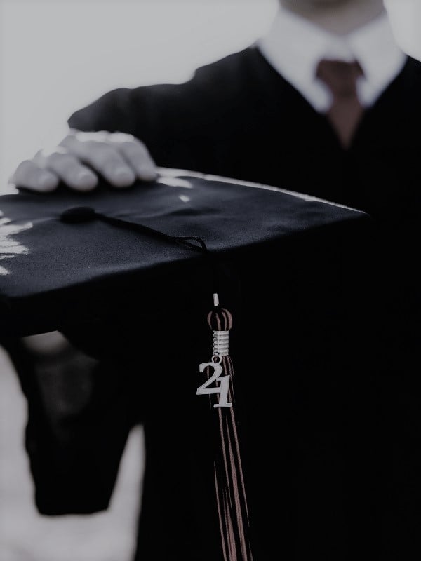 male student in graduation gown holding cap